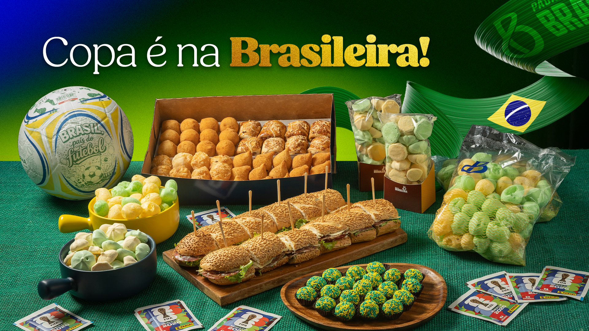 Mesa da Padaria Brasileira com combos para a torcida: bola de futebol, mini salgados, lanche de metro, pães de queijo e brigadeiros verde e amarelo, com a frase Copa é na Brasileira.